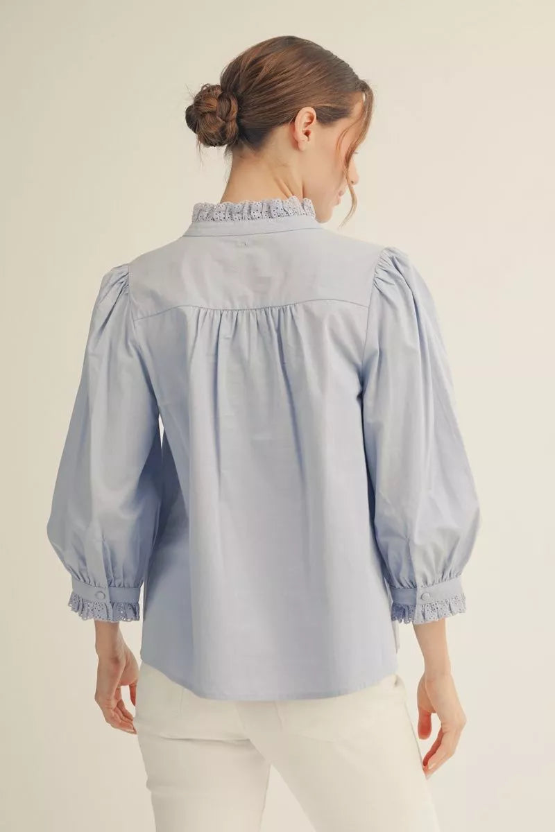 Woman wearing a light blue blouse with puffed sleeves on a plain background