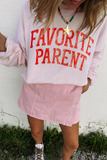 Person wearing a pink sweatshirt with 'FAVORITE PARENT' text against a white wall.