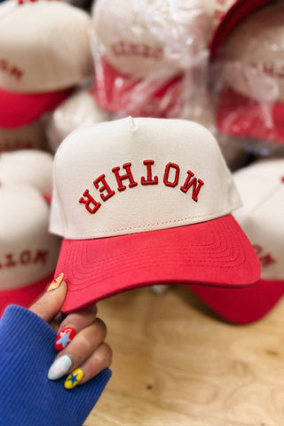 Red and white cap with 'MOTHER' text held by a hand with colorful nail polish.
