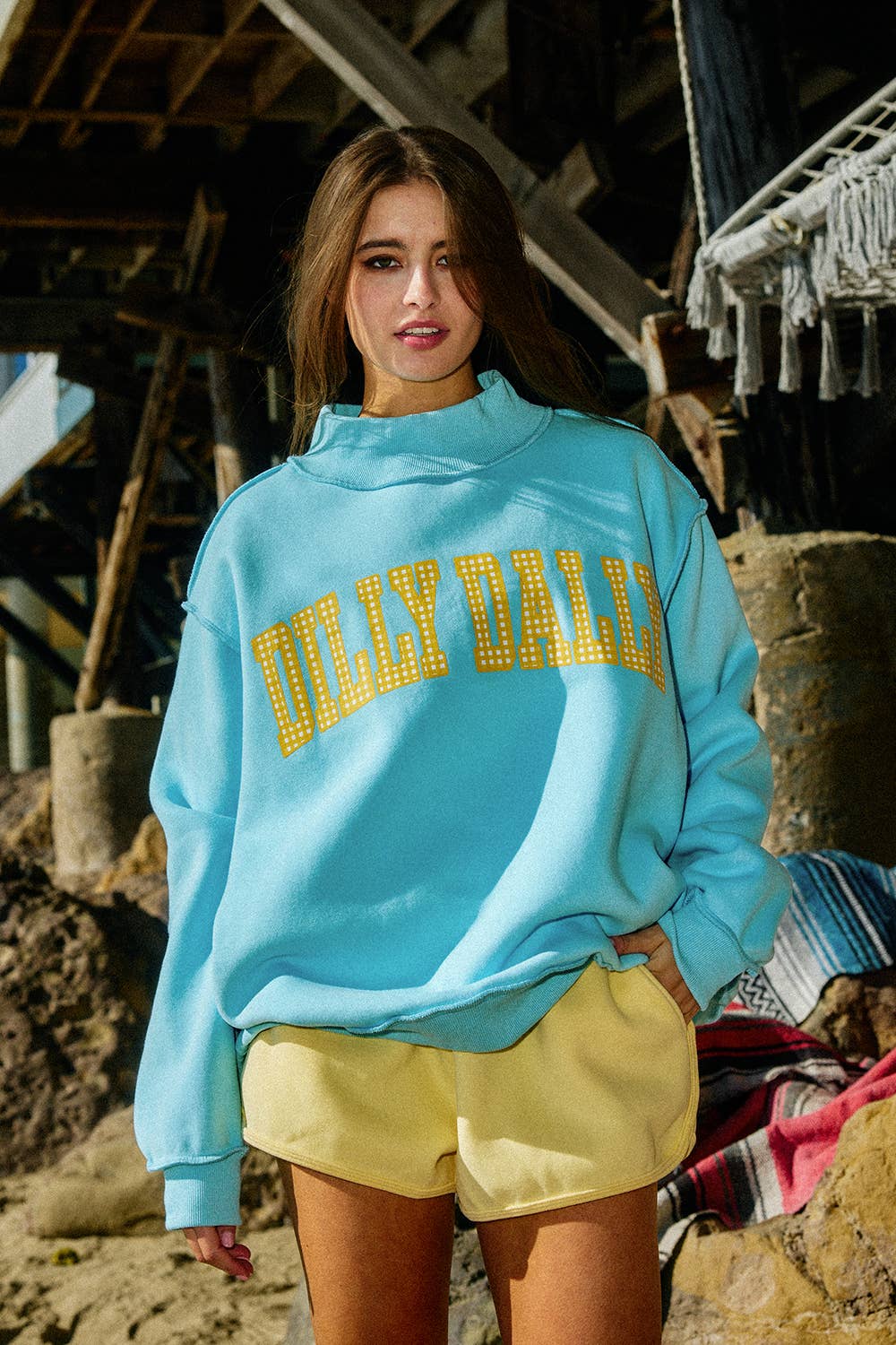 Woman wearing a light blue sweatshirt with 'Dilly Dally' text, standing outdoors.