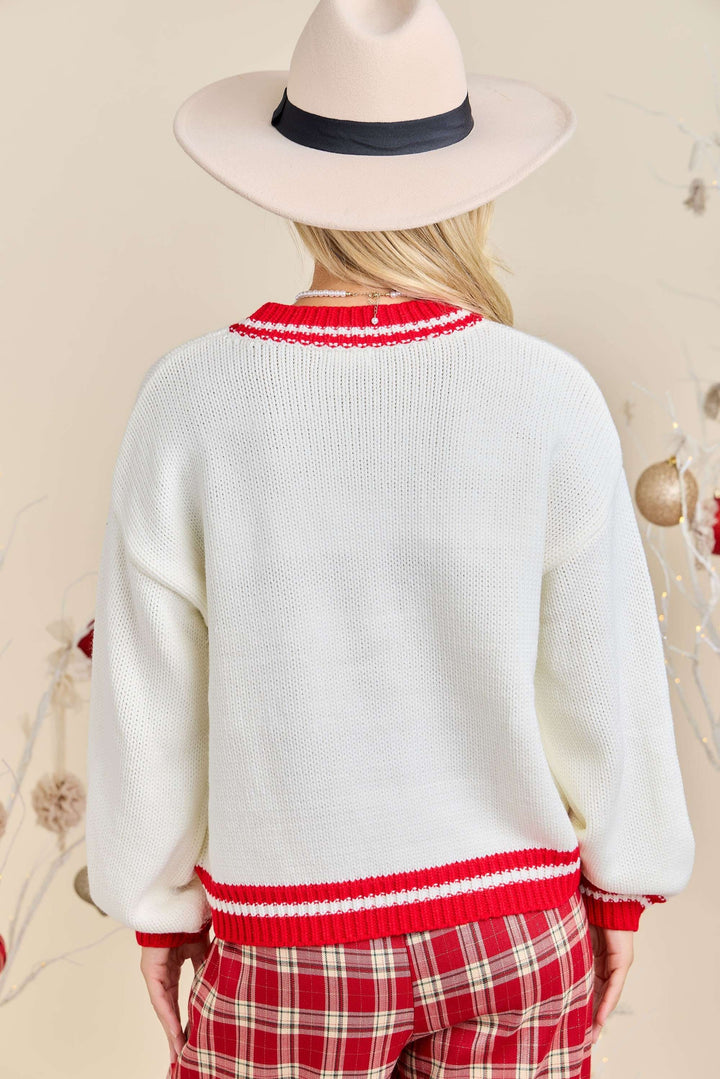 Person wearing a white sweater with red trim and plaid pants, standing against a neutral background.
