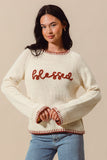Woman wearing a cream sweater with 'blessed' in red text on a beige background