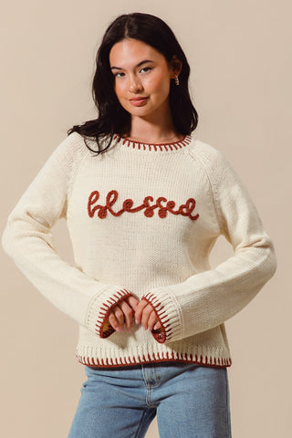Woman wearing a cream sweater with 'blessed' in red text on a beige background
