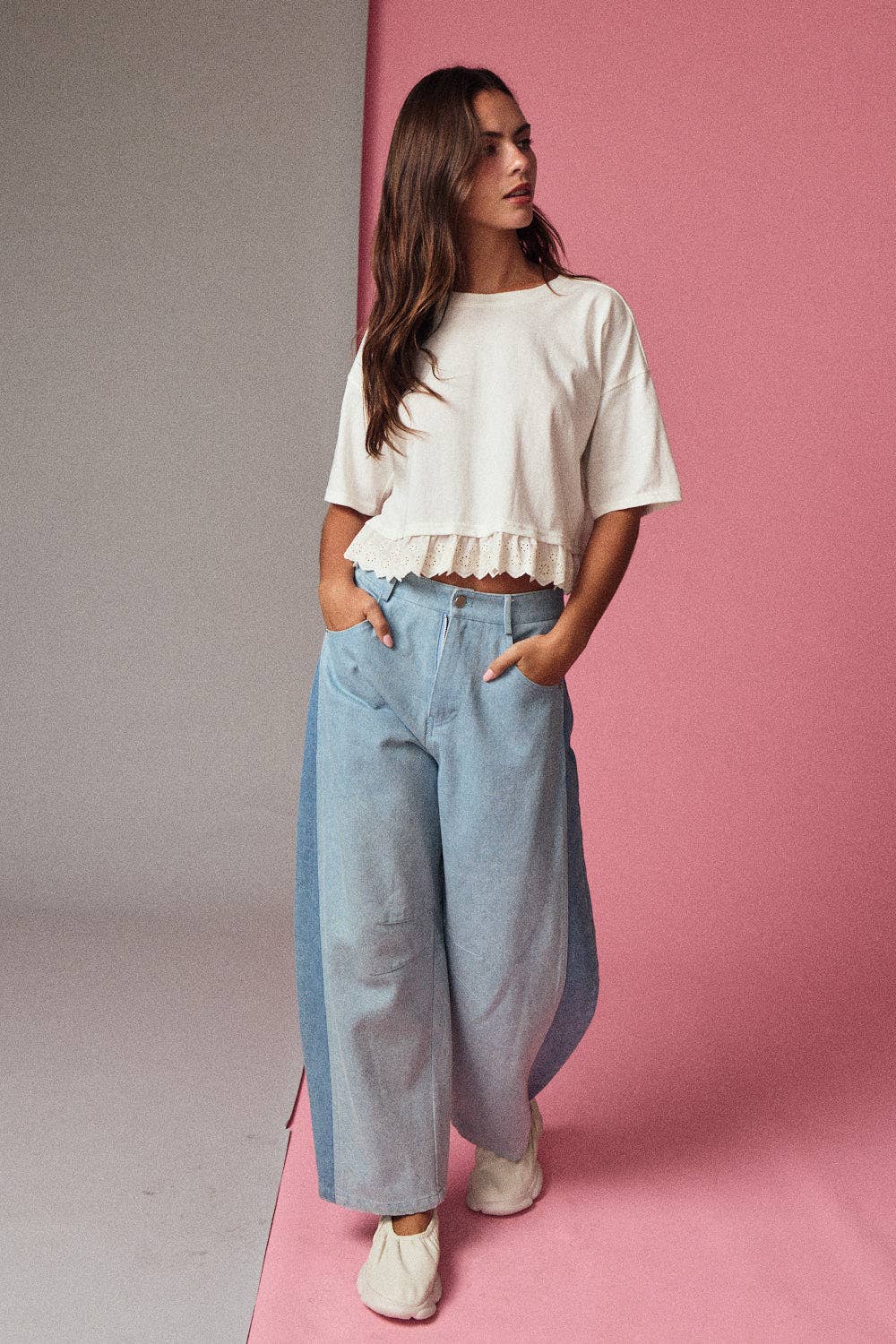 Woman wearing a white top and light blue jeans against a pink background