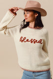 Woman wearing a cream sweater with 'blessed' text and a beige hat against a beige background