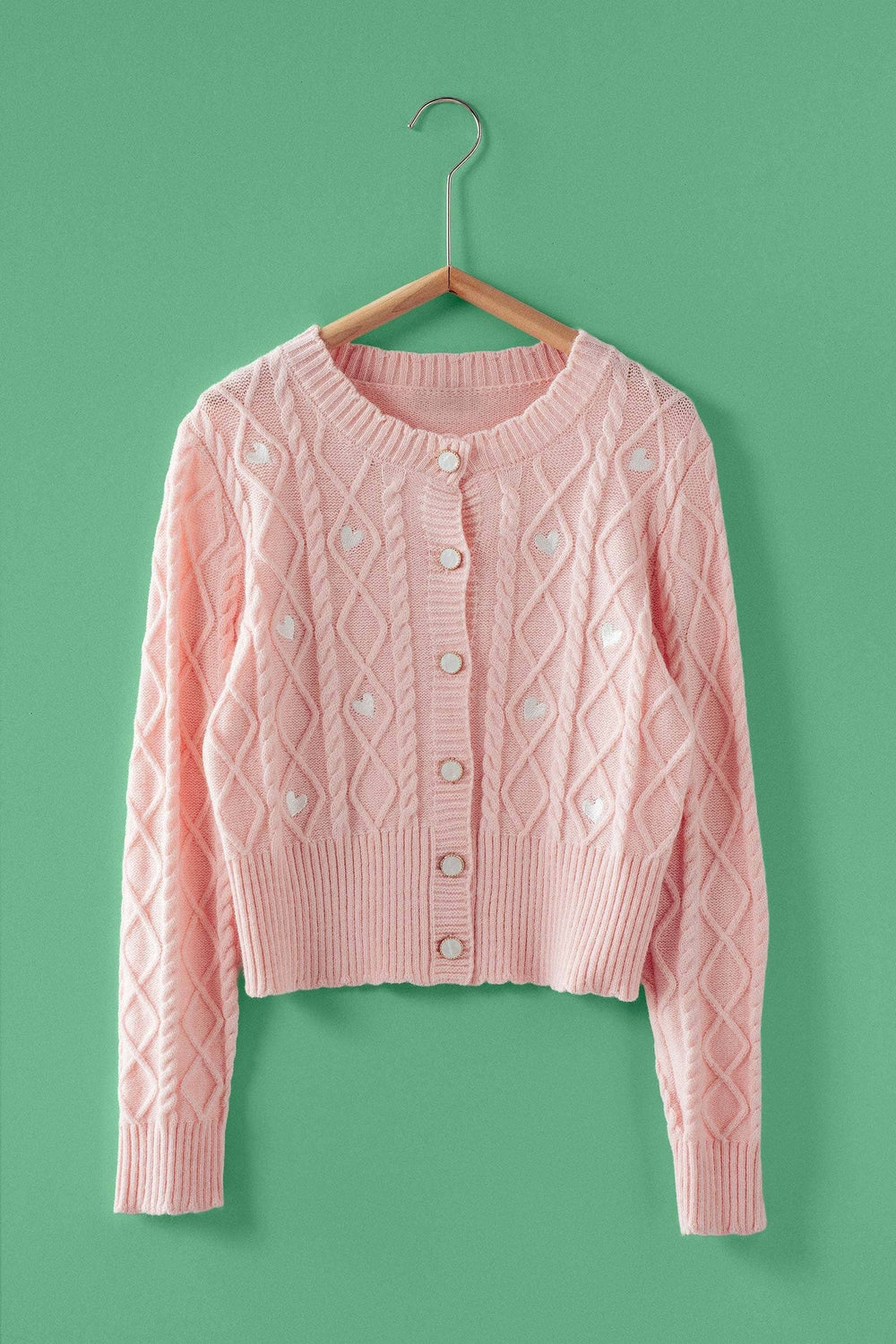 Pink cable knit cardigan on a hanger against a green background