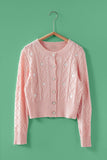 Pink cable knit cardigan on a hanger against a green background