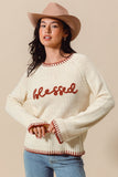 Woman wearing a cream sweater with 'blessed' text, blue jeans, and a beige hat on a beige background