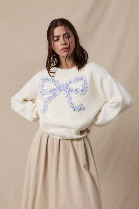 Woman wearing a white sweater with a blue bow design against a beige background
