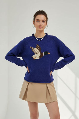 Woman wearing a blue sweater with a duck design and a beige skirt on a white background