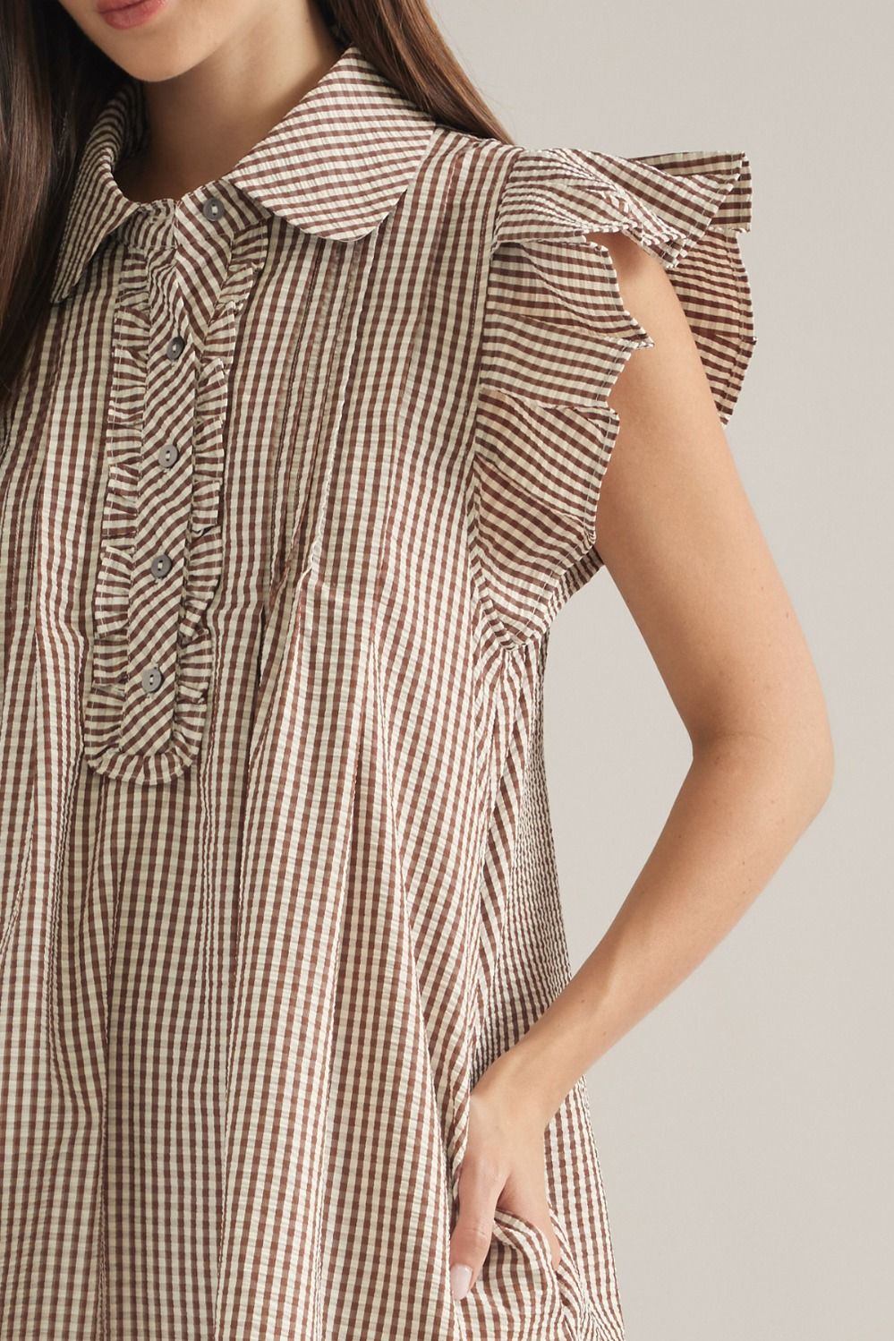 A close-up of a woman wearing a brown and beige gingham check dress with ruffled details on the collar and sleeve.