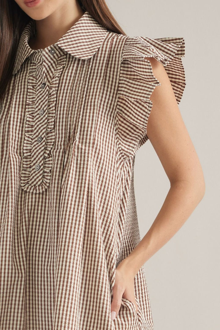 A close-up of a woman wearing a brown and beige gingham check dress with ruffled details on the collar and sleeve.
