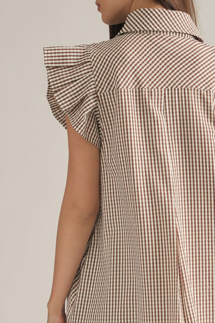 Close-up back view of a model wearing a brown and beige gingham shirt dress with ruffled cap sleeves and a collar, against a light beige background.