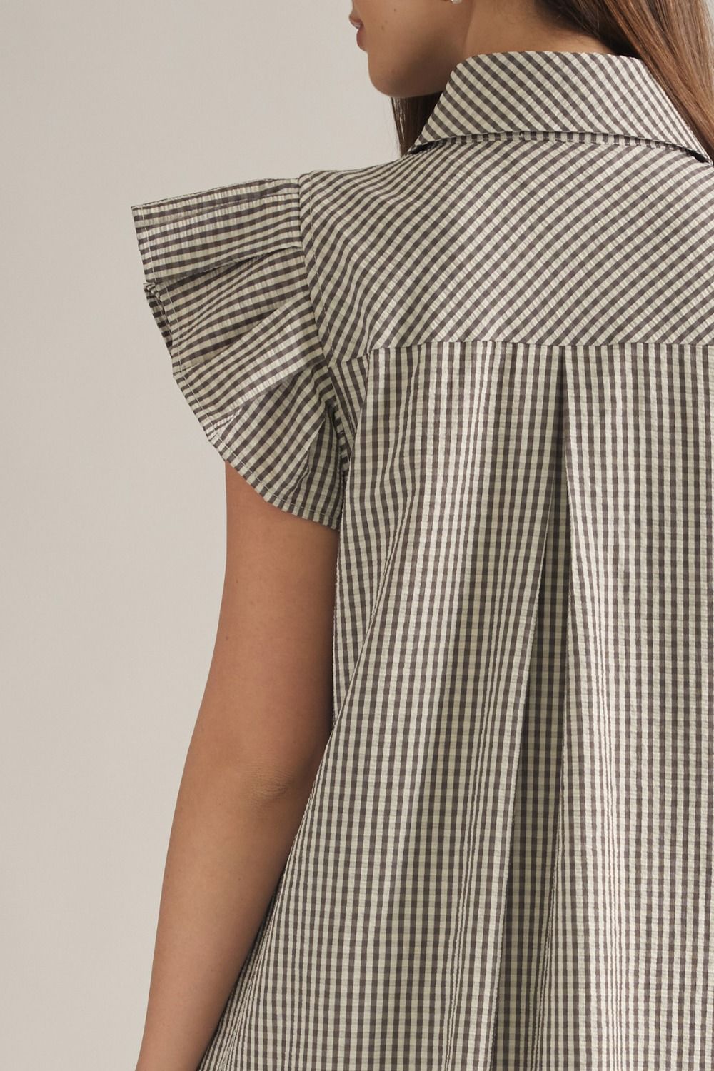 Close-up of a model wearing a short-sleeve collared shirt dress with a brown and white gingham pattern and ruffled cap sleeves.