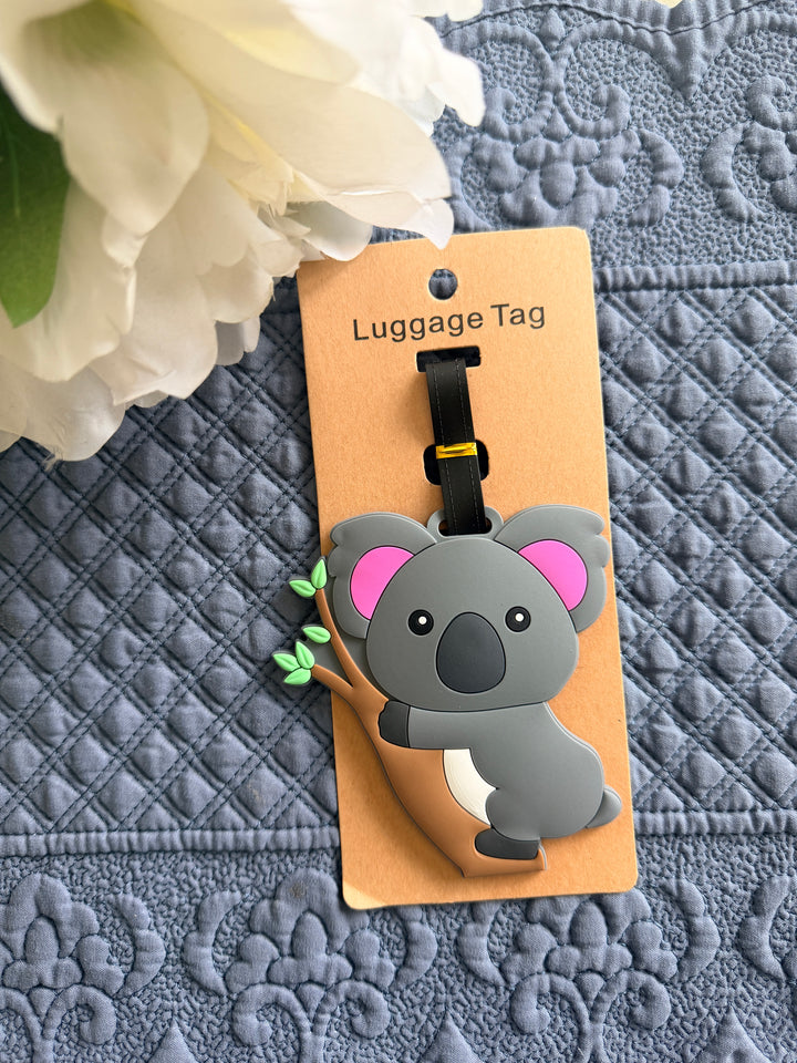Luggage tag shaped like a koala on a cardboard backing with flowers in the background
