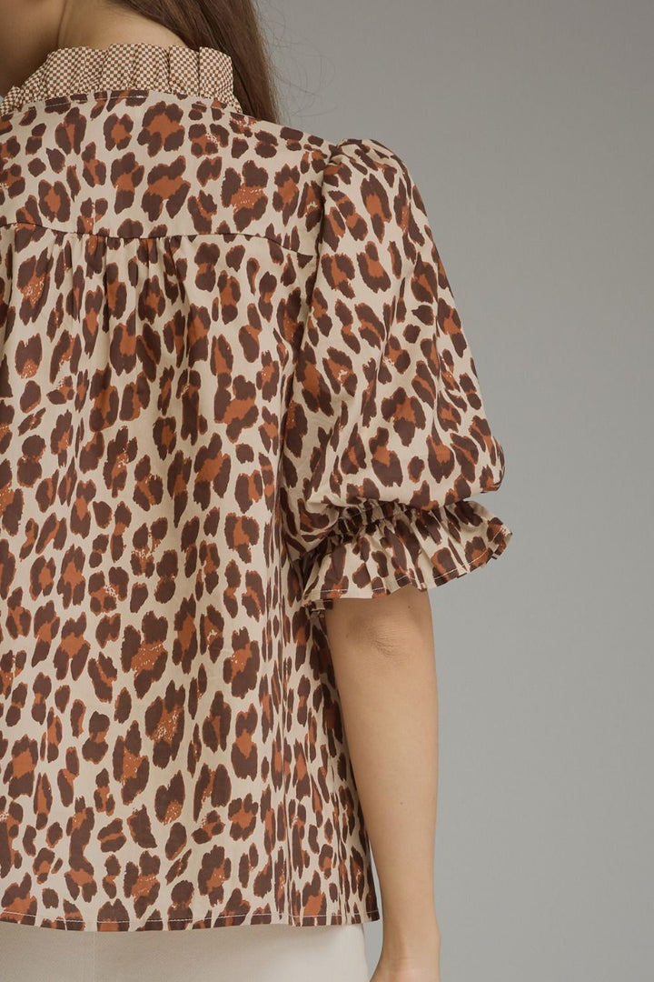 A close-up of a model wearing a leopard print blouse with puff sleeves and a ruffled collar, shown from the back against a solid gray background.