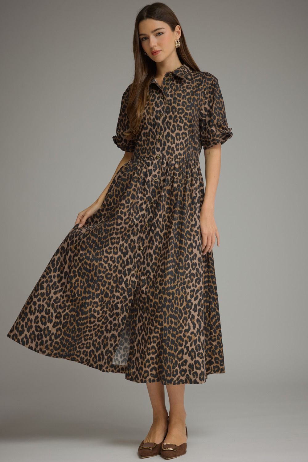 A woman modeling a leopard-print midi dress with short puff sleeves, a collared neckline, and a gathered waist, photographed against a plain light gray studio background.
