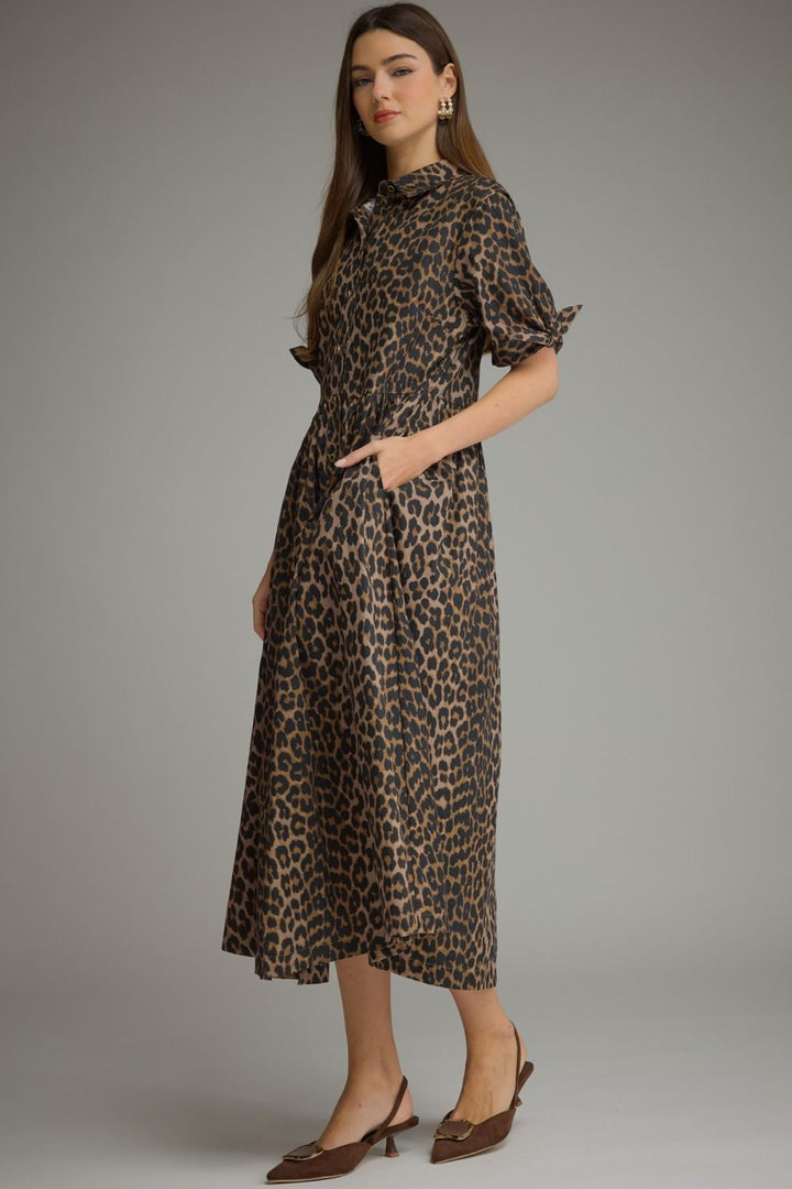A woman modeling a leopard-print midi dress with puff sleeves and side pockets, paired with brown pointed-toe heels, against a solid gray studio background.