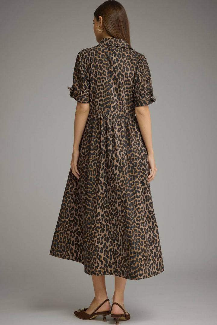 A woman viewed from the back wearing a leopard-print midi dress with short ruffled sleeves and brown heeled sandals, photographed against a plain gray studio background.