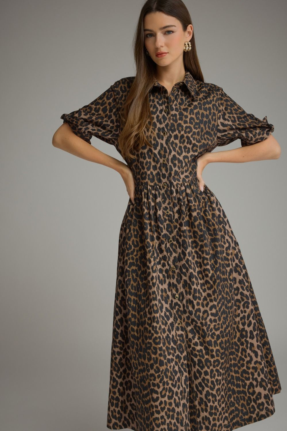 A woman modeling a leopard-print midi dress with puff sleeves, a collared neckline, and a gathered waist, photographed against a plain gray studio background.