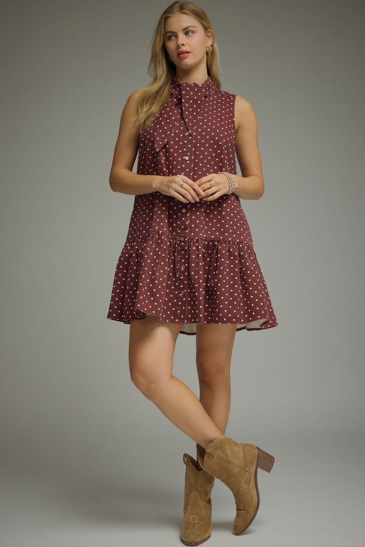 Woman wearing a maroon dress with white polka dots and brown boots on a gray background
