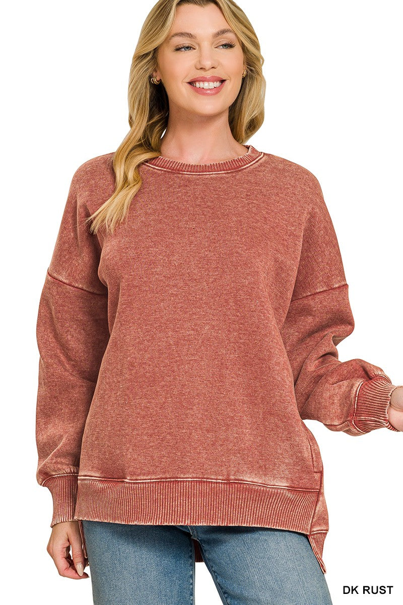 A woman wearing a washed, heathered dusty rose crewneck sweatshirt with ribbed cuffs and hem, paired with blue jeans, against a plain white background.