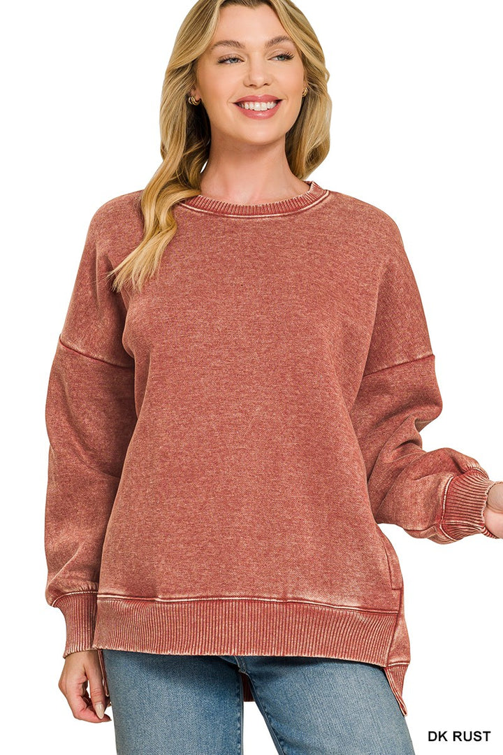 A woman wearing a washed, heathered dusty rose crewneck sweatshirt with ribbed cuffs and hem, paired with blue jeans, against a plain white background.