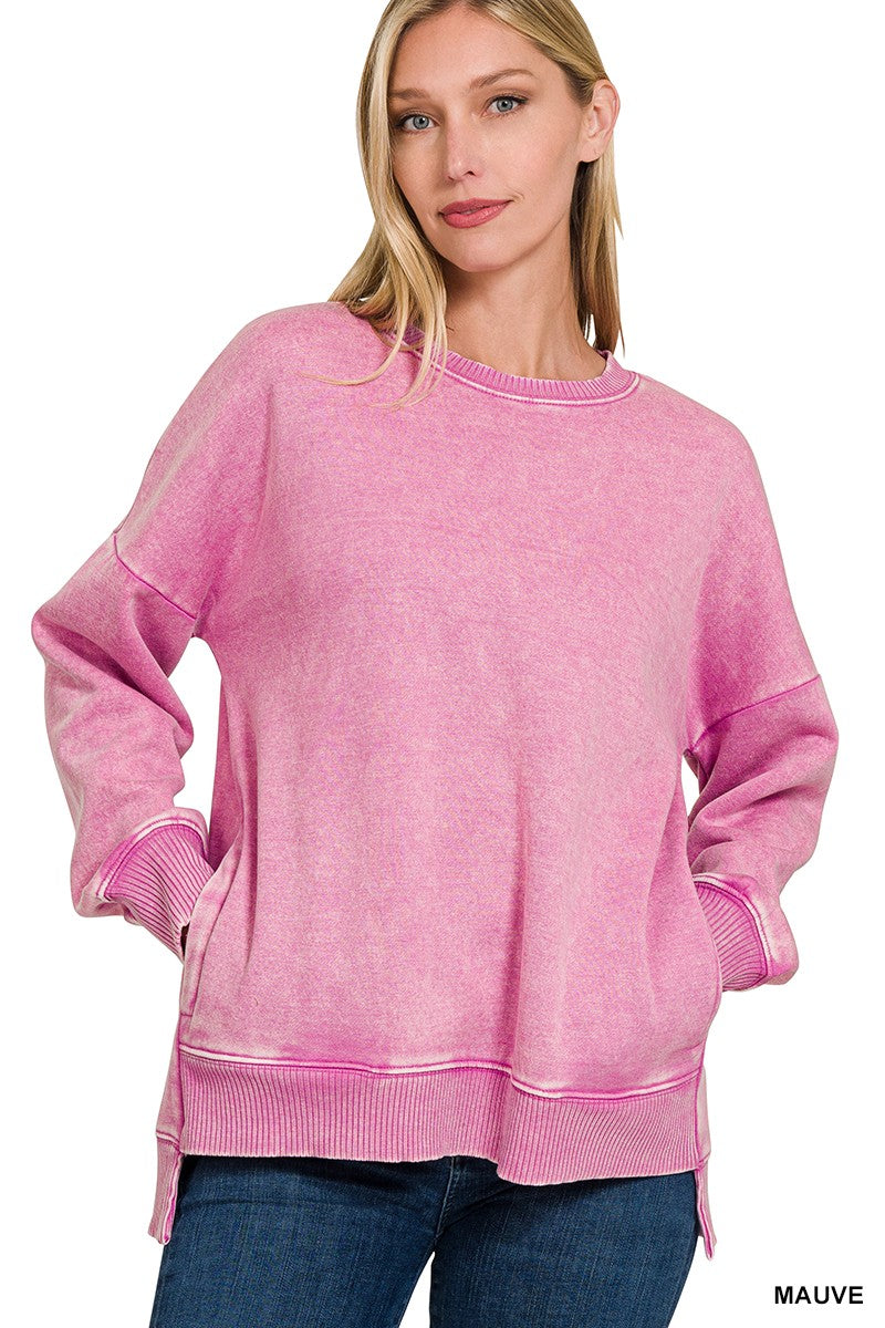 A woman wearing a pink acid-wash crewneck sweatshirt with ribbed cuffs and hem, paired with blue jeans, against a plain white background.