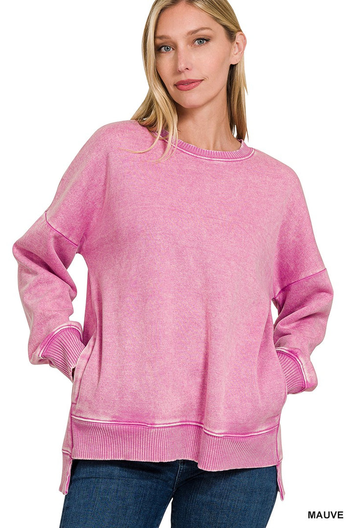 A woman wearing a pink acid-wash crewneck sweatshirt with ribbed cuffs and hem, paired with blue jeans, against a plain white background.