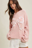 Woman wearing a pink sweater with a lace bow design on a beige background