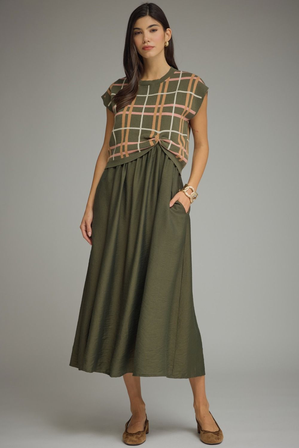 Woman wearing a green dress with a plaid top against a gray background