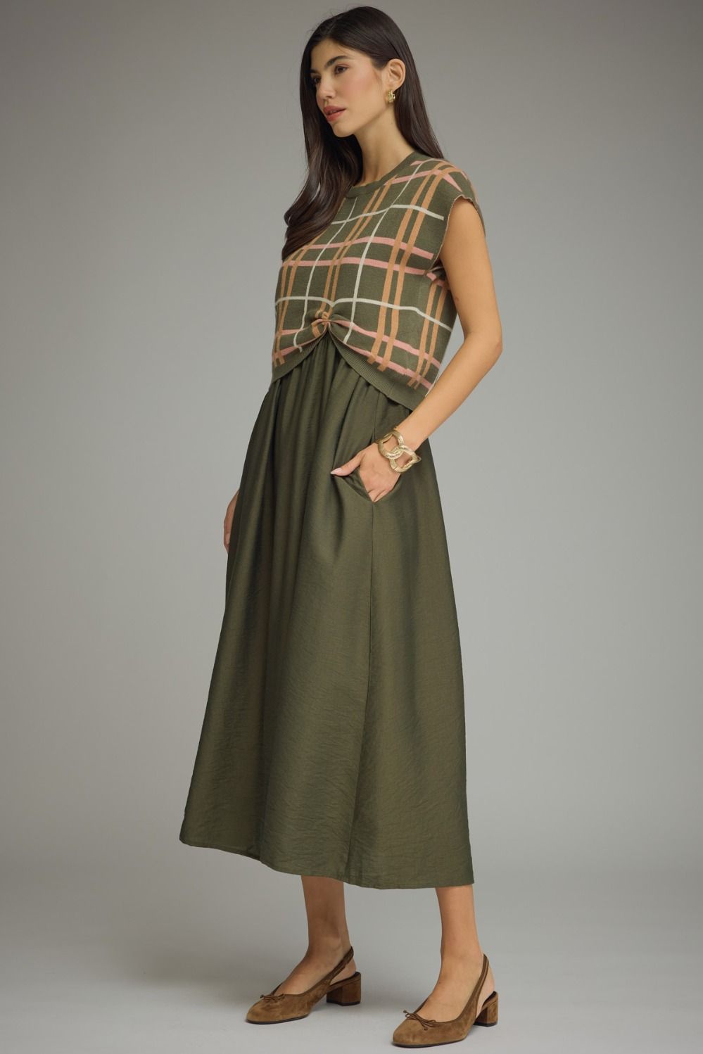 Woman wearing a green dress with a plaid top against a gray background
