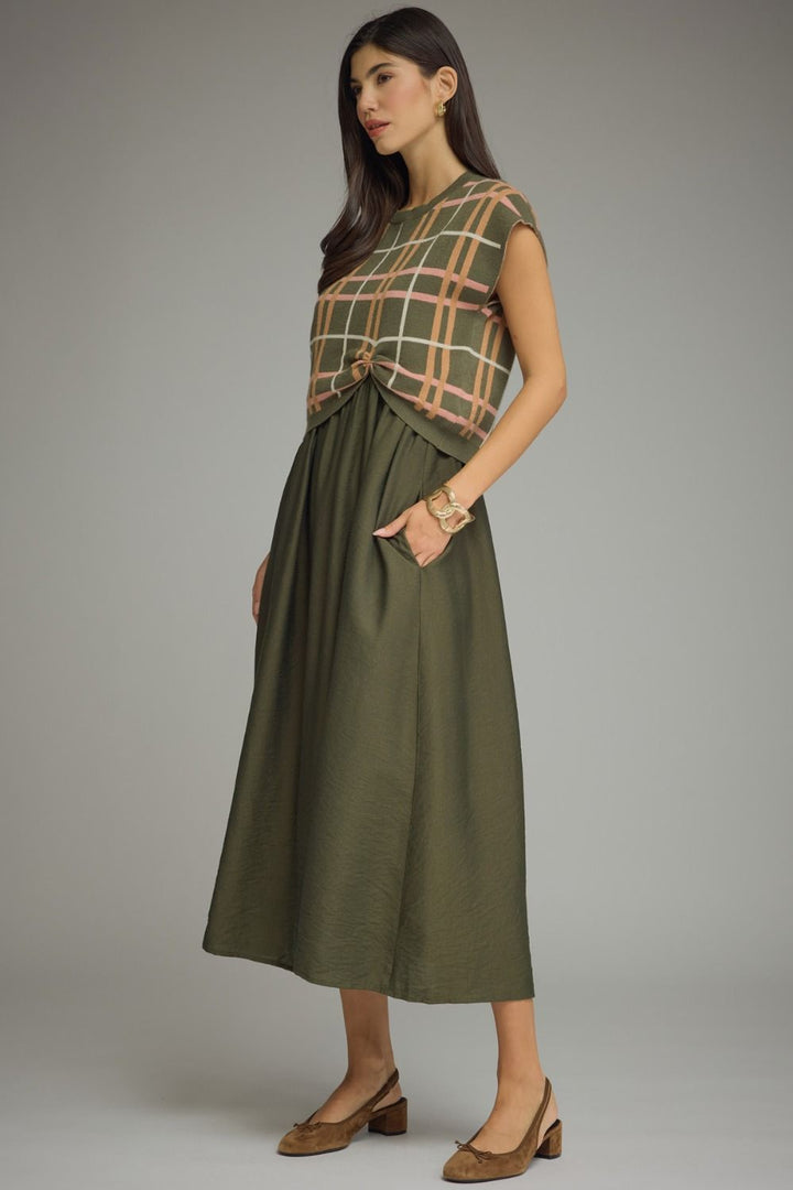 Woman wearing a green dress with a plaid top against a gray background