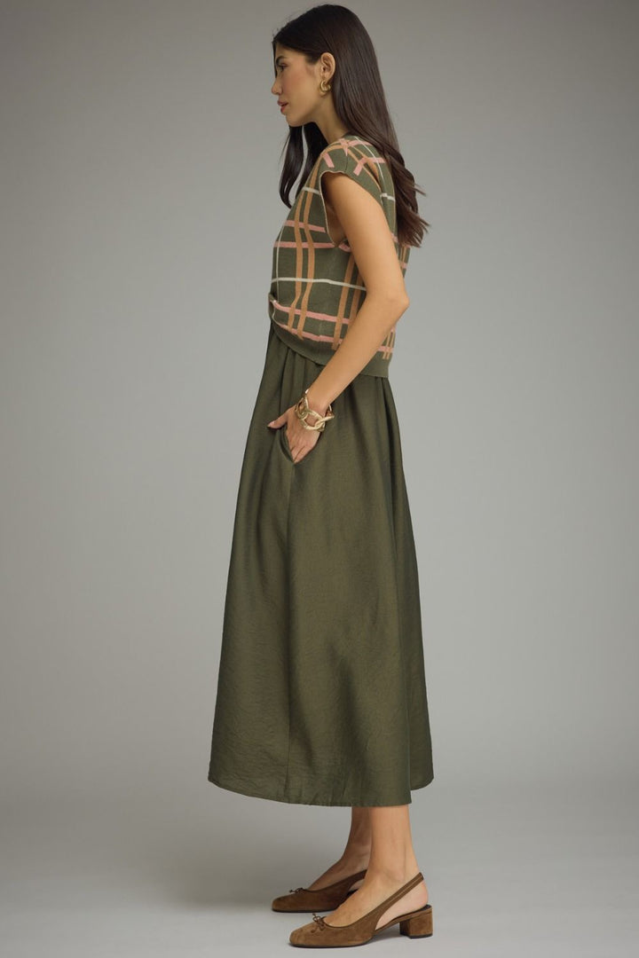 Woman wearing a green dress with a plaid top against a gray background