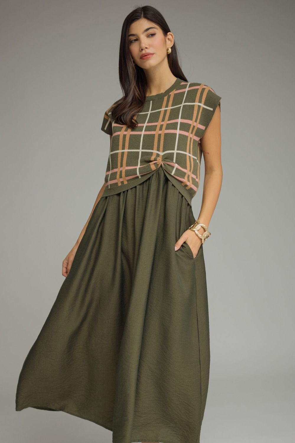 Woman wearing a green dress with a plaid top against a gray background