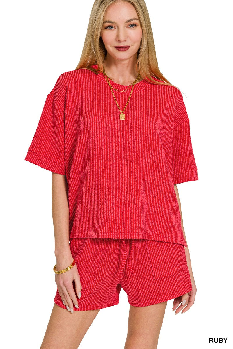 Woman wearing a red ribbed outfit with a necklace on a white background