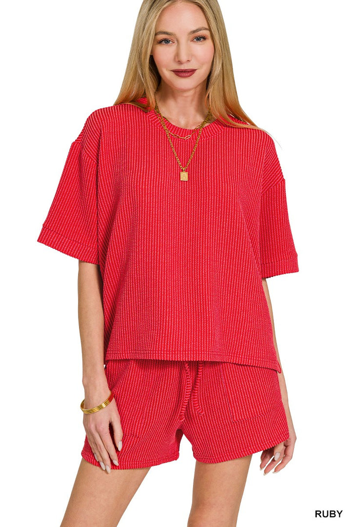 Woman wearing a red ribbed outfit with a necklace on a white background