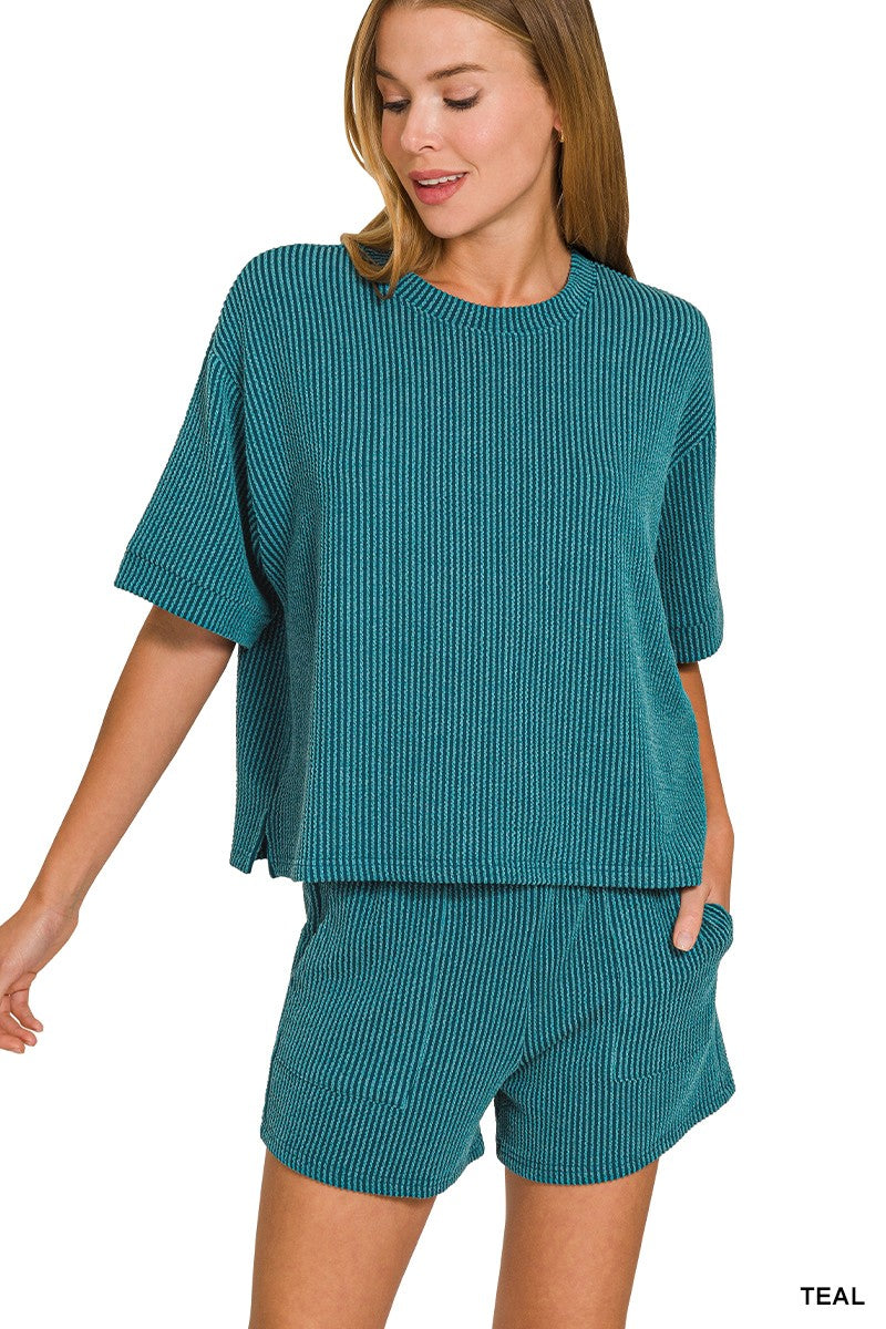 A woman modeling a matching teal ribbed knit lounge set consisting of a short-sleeve top and shorts, shown against a plain white background.