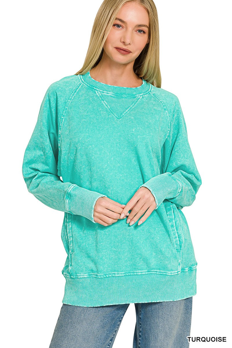 A woman modeling a turquoise long-sleeve crewneck sweatshirt with a washed, faded texture, paired with blue jeans against a plain white background.