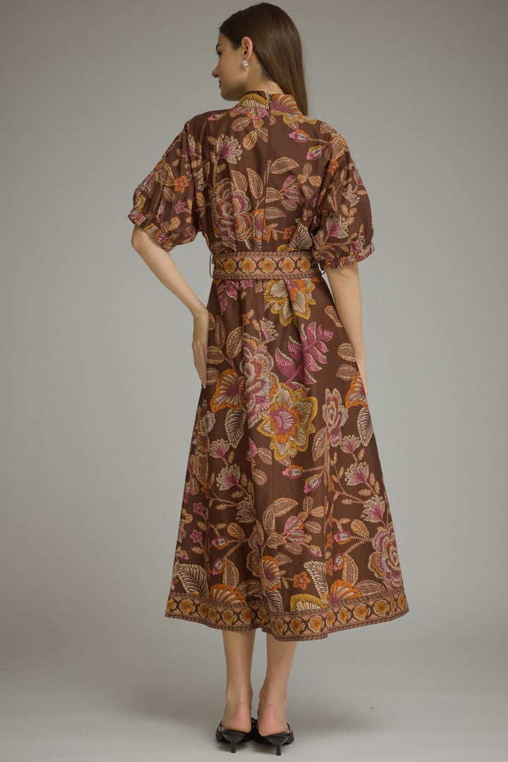 A woman modeling a brown midi dress with a colorful floral and butterfly print, shown from the back against a neutral gray studio background.