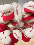 Stack of white and red caps with 'MOTHER' text on a wooden surface.