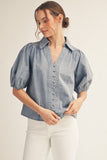 Woman wearing a blue denim blouse with puff sleeves on a beige background