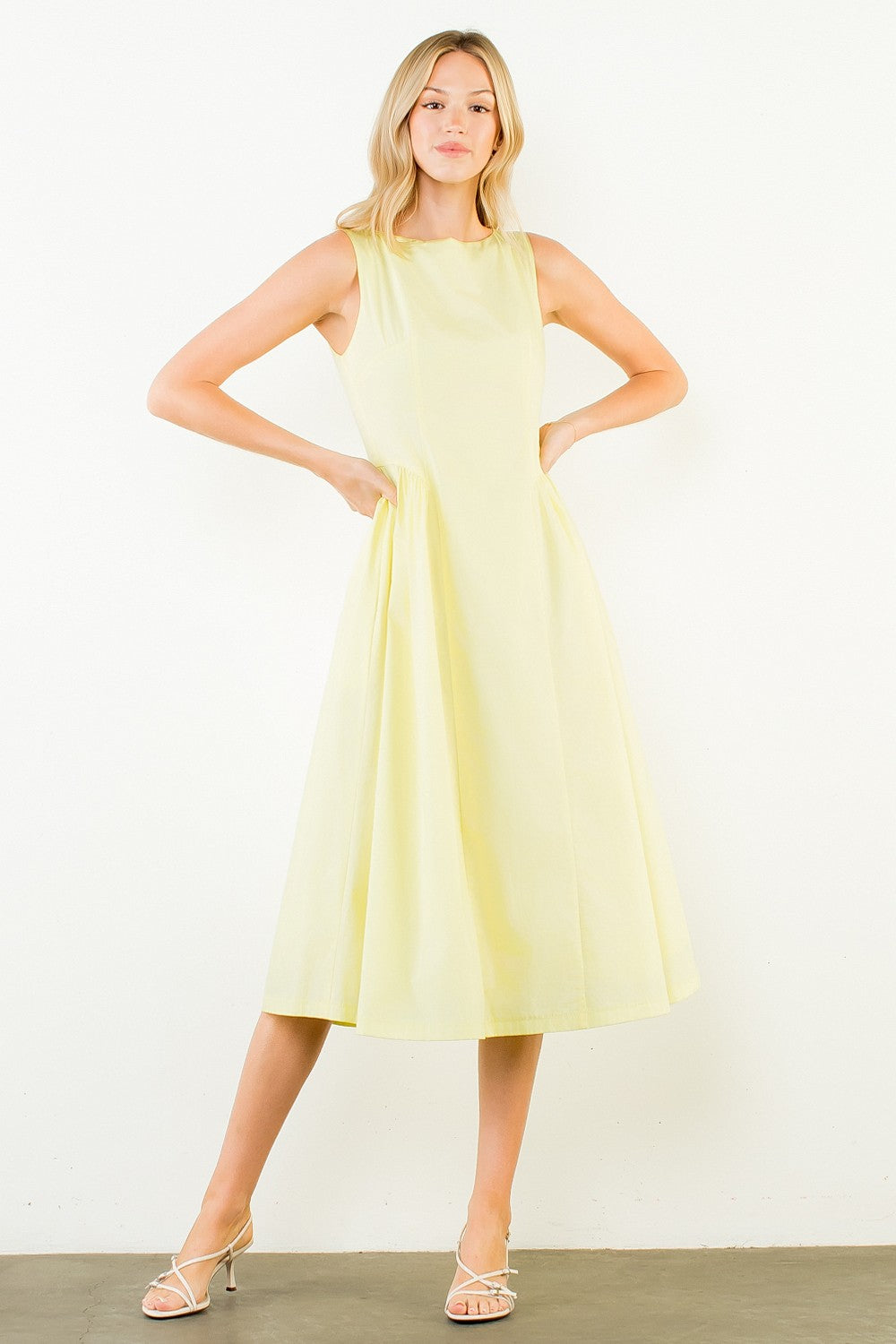 Woman in a light yellow dress standing outdoors with plants around