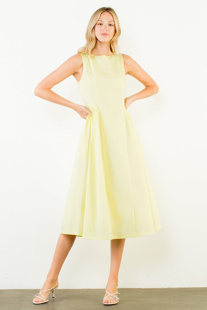 Woman in a light yellow dress standing outdoors with plants around