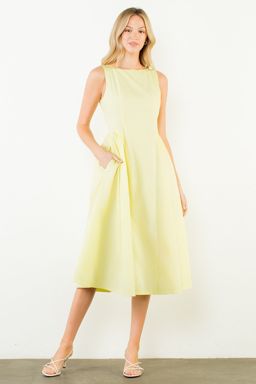 Woman in a light yellow dress standing outdoors with plants around