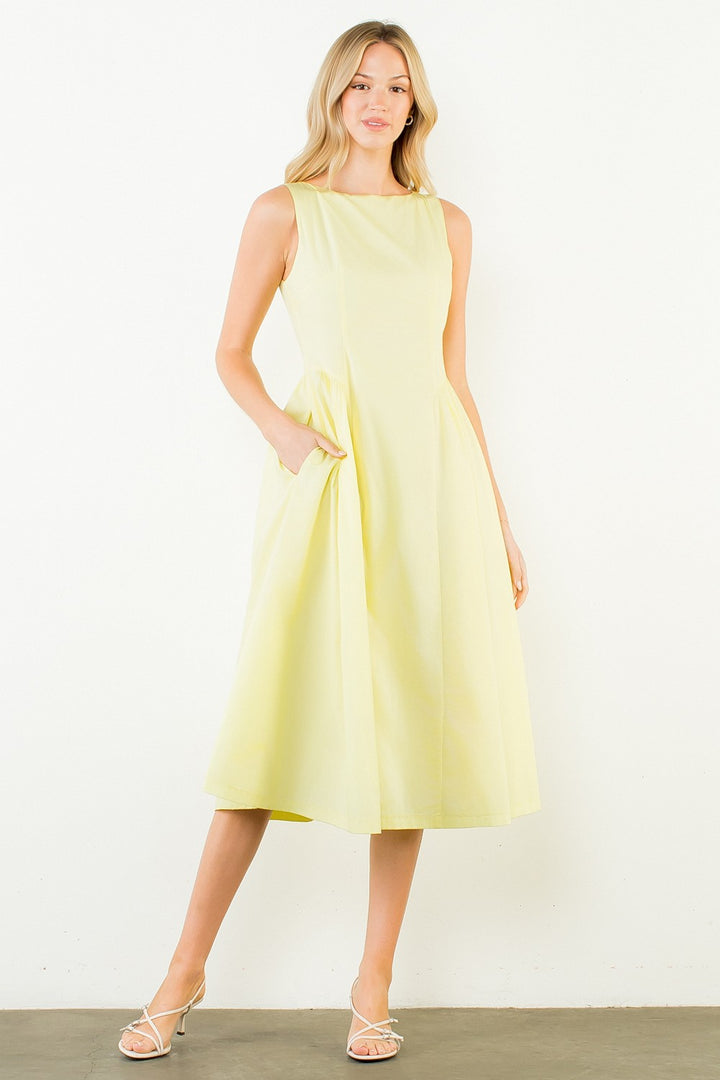 Woman in a light yellow dress standing outdoors with plants around