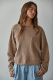 Woman wearing a brown sweater and blue jeans against a plain background