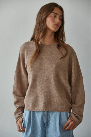Woman wearing a brown sweater and blue jeans against a plain background