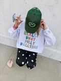 Person wearing a colorful sweatshirt and green cap, standing against a light-colored wall.