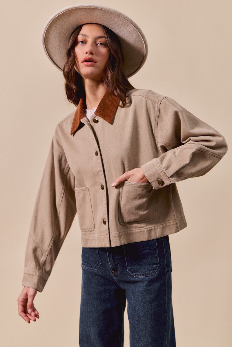 Woman wearing a beige jacket with leather accents and a hat on a beige background